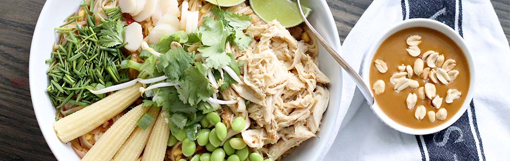 Bowl of Pad Thai noodles topped with shredded chicken, corn, edamame and cilantro. Peanut sauce served on the side.